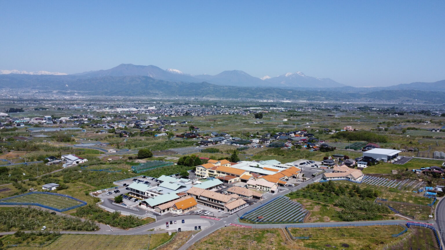 施設全体の鳥瞰図。周辺の田園風景と遠景の山々が見える。
