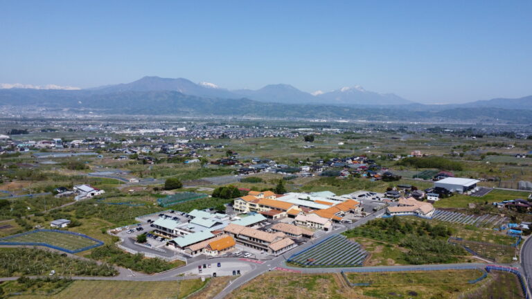 施設と周辺環境を上空から捉えた景観写真。農村地帯と山々を背景に